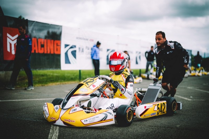 A mechanic pushes Khalid's number 542 FIA Karting Academy kart to the grid under a stormy sky